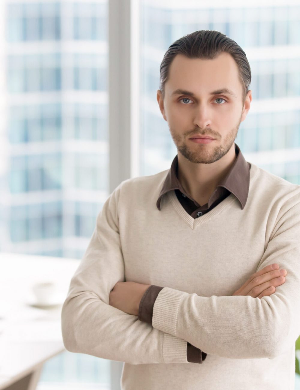 Portrait of young businessman standing in office with arms crossed. Ambitious successful entrepreneur, small business owner or company director posing looking at camera with serious facial expression